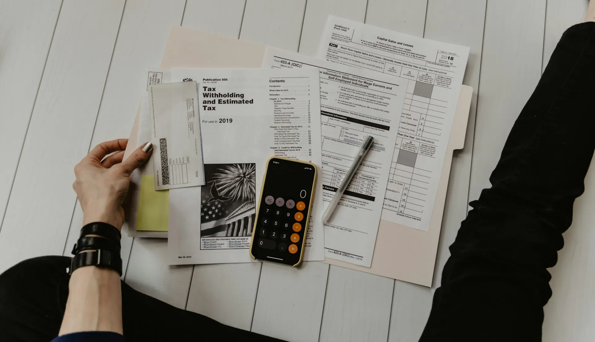 Documentos de impuestos y formularios financieros sobre una mesa, con una calculadora y una persona revisándolos